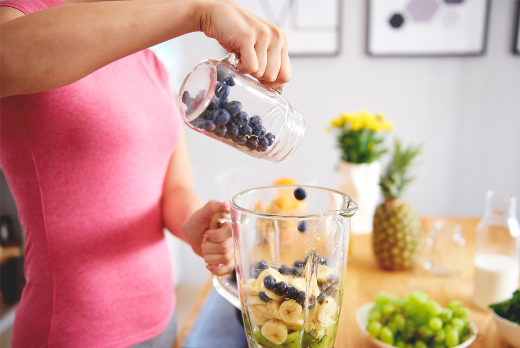 Una donna mette vari tipi di frutta nel frullatore.